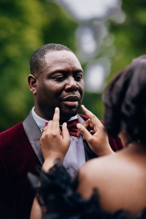 Someone adjusts a burgundy suit and bowtie during an elegant outdoor photoshoot.