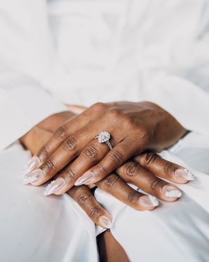 Close-up shots of elegant diamond engagement ring on well-manicured hands with white nail polish against white background.