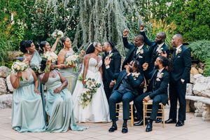 Wedding party in sage green dresses and black suits posing together outdoors.
