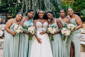 Wedding party wearing mint green bridesmaid dresses and white bridal gown pose together holding floral bouquets outdoors.