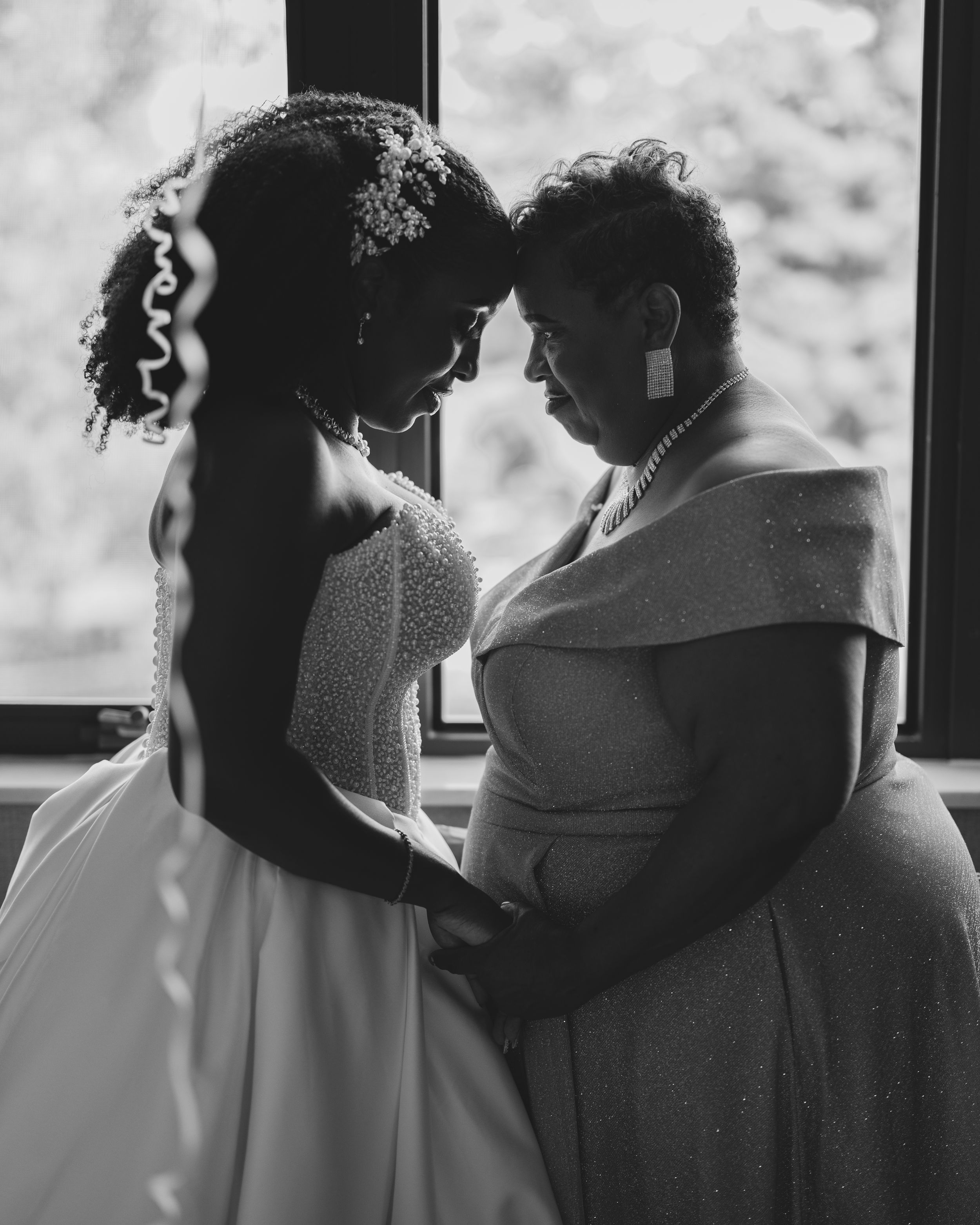 Intimate black and white portrait of two people sharing a tender moment in front of a window.