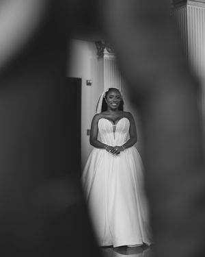 Elegant wedding dress displayed in a white room with dramatic lighting and vignette effect.