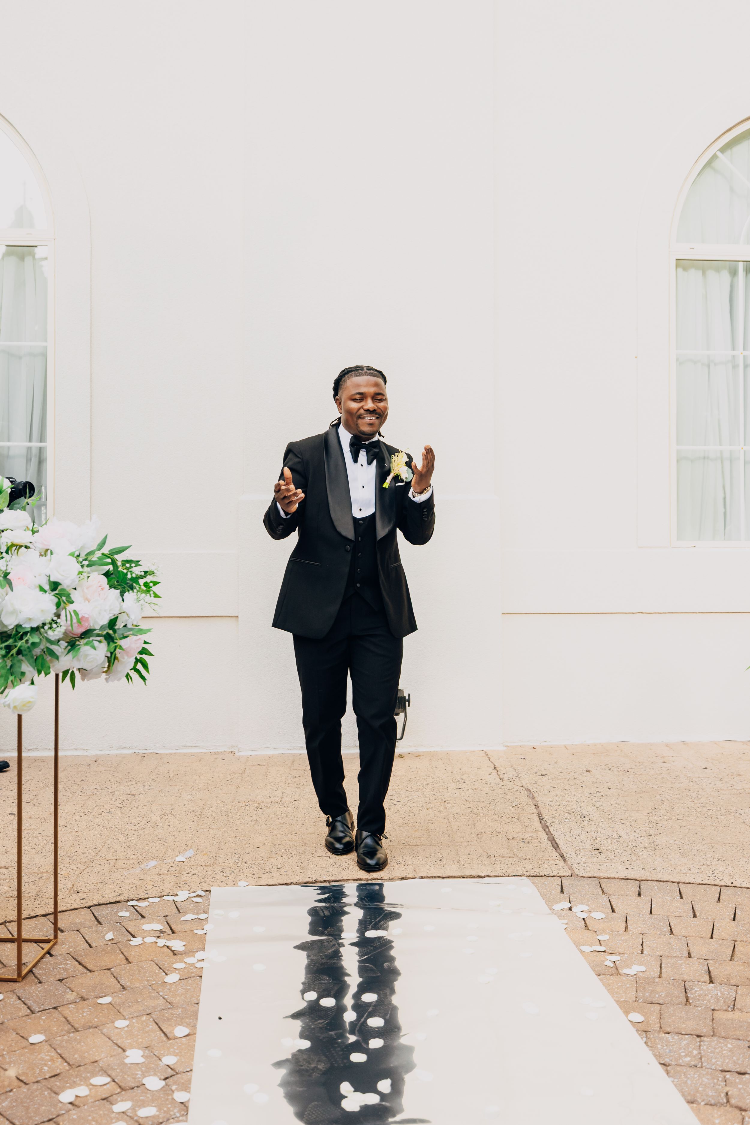 Three shots show someone joyfully jumping and posing in a formal black tuxedo on a paved walkway.
