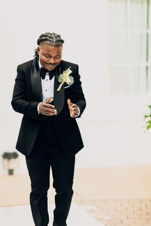 Groomsman in black tuxedo takes a sip from a champagne glass during wedding celebration.