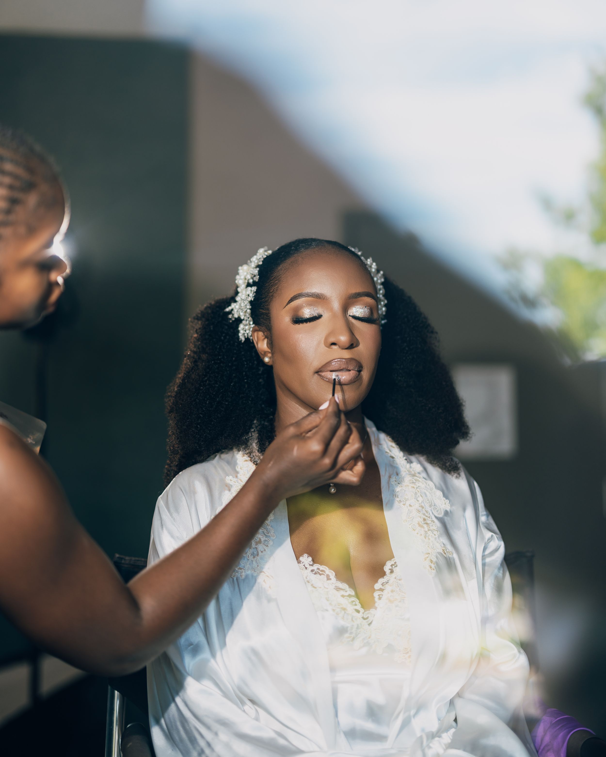 Wedding preparation scene with person in white robe getting makeup professionally applied in serene setting.
