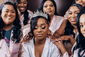 A bridal party in pink robes surrounds the bride wearing a crystal crown.