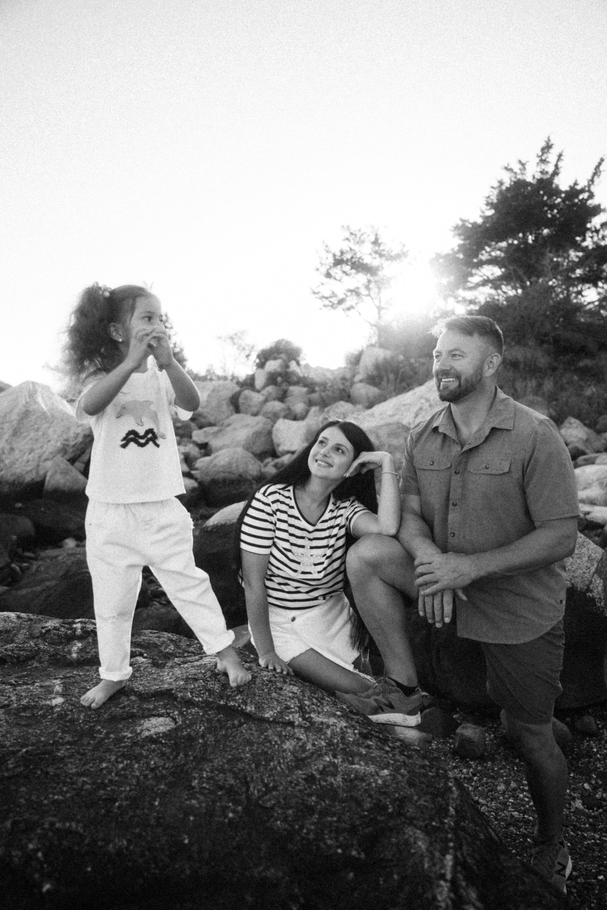 A joyful family moment captured in black and white as they laugh together on rocky terrain at sunset.