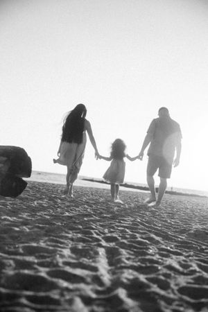 A family silhouetted against bright sky walking hand in hand on a sandy beach in black and white.
