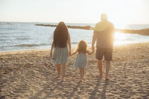 Family walking together on sandy beach at sunset as waves crash on shoreline in background.