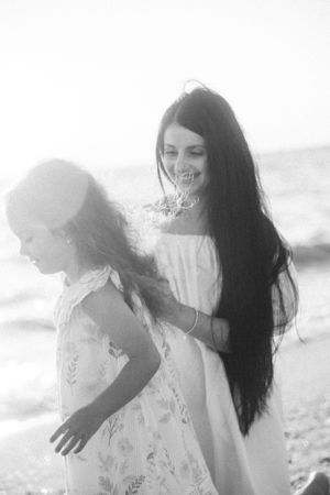 Two figures in white dresses standing on a beach in a dreamy black and white photograph.