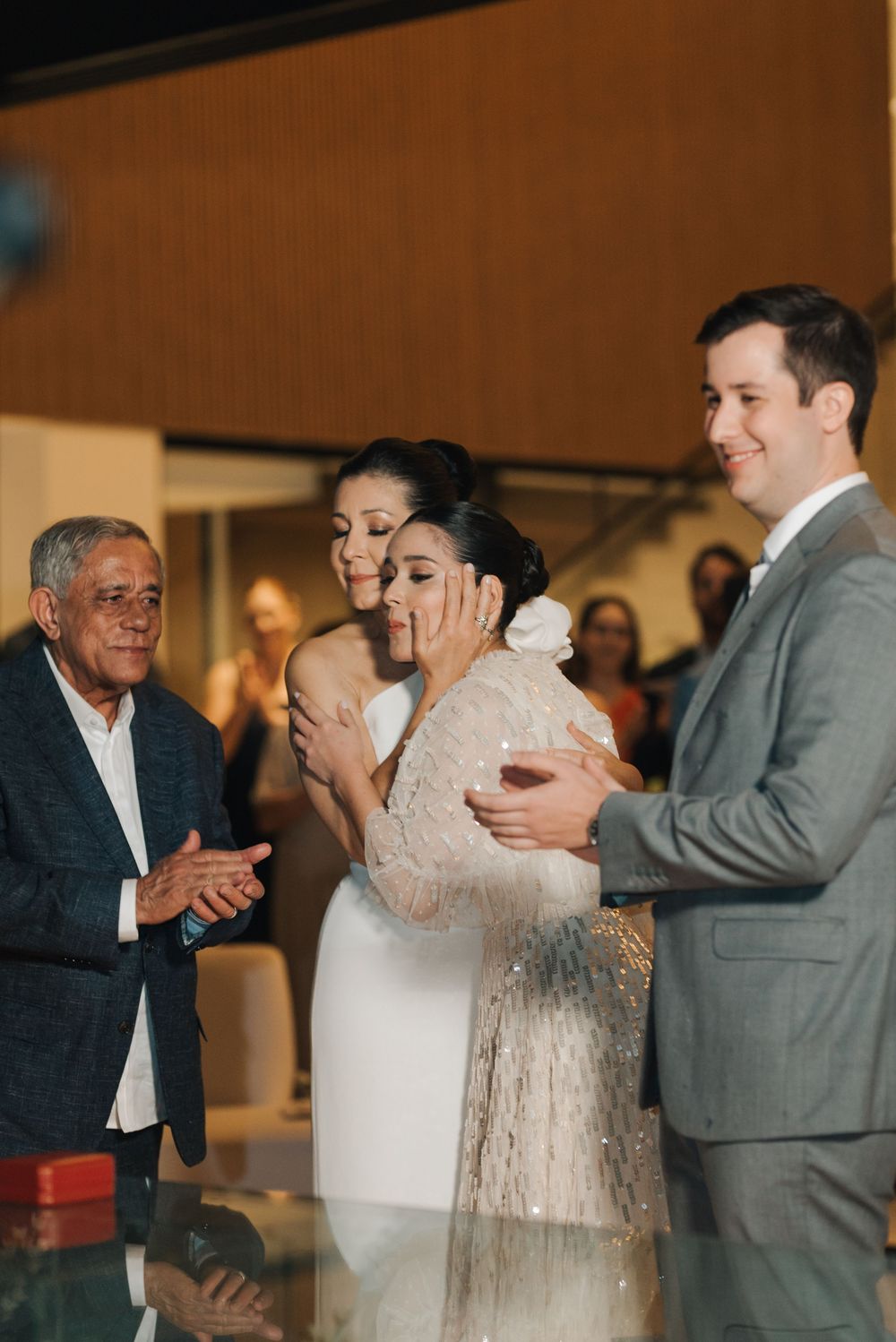 Wedding reception guests celebrate and embrace during an emotional moment at an indoor venue.