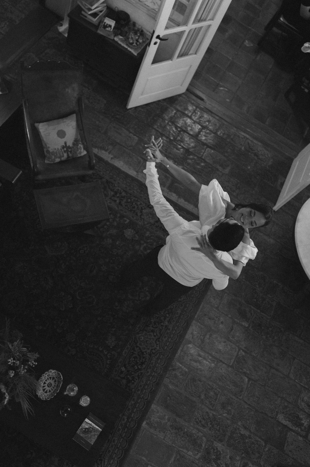 Aerial black and white photo of a person in white outfit dancing in a rustic room with wooden floors.