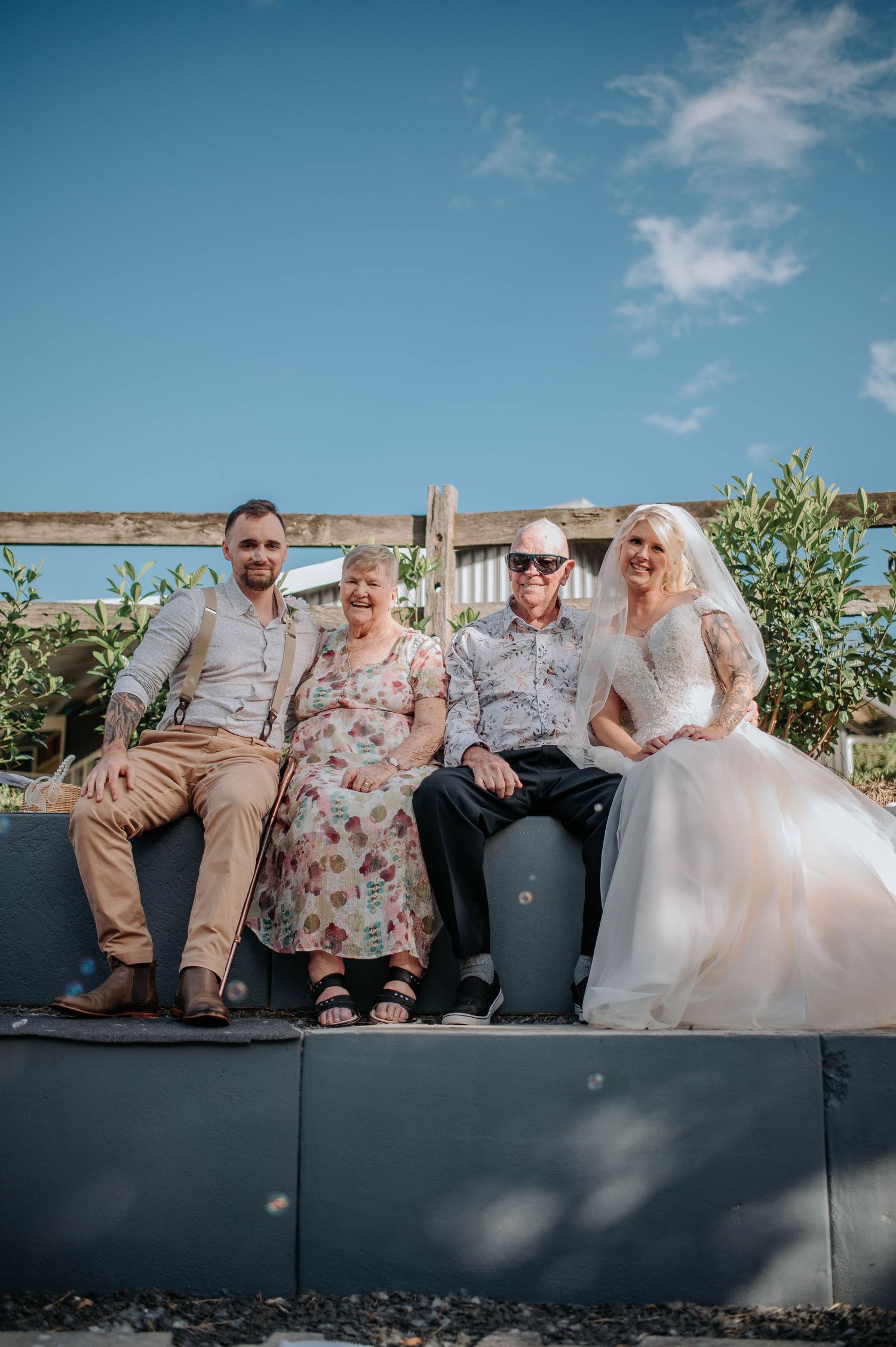 Wedding party poses together on outdoor bench with scenic view in background.
