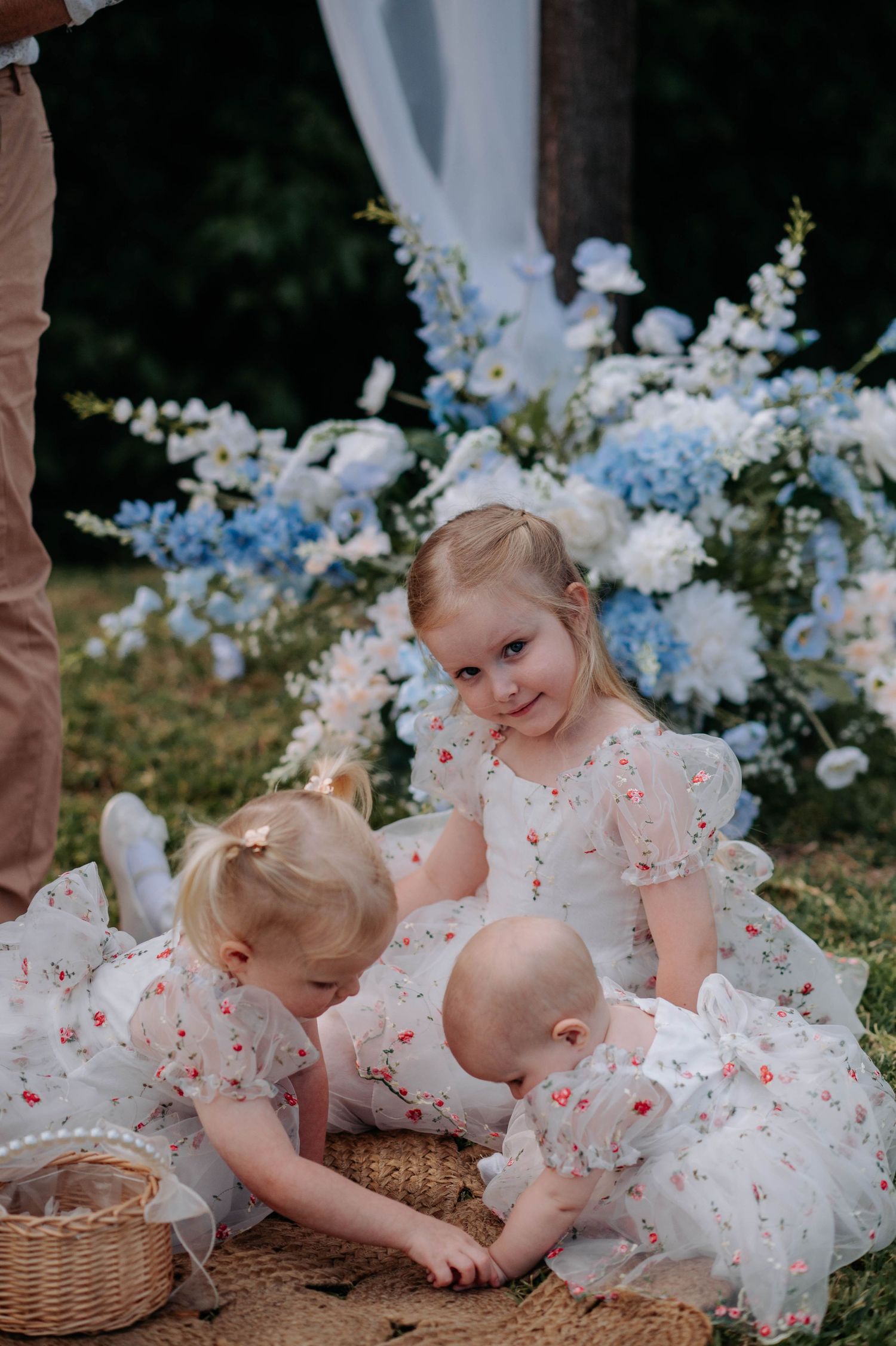 Children in matching floral dresses play with baskets near blue and white flower arrangements.