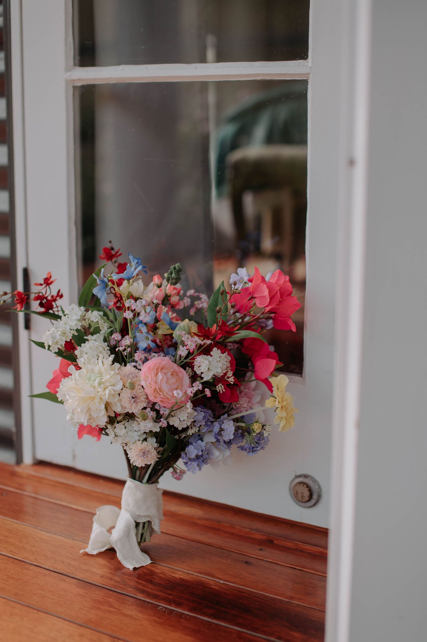 Colorful floral arrangement with pink and purple blooms in mason jar by window.