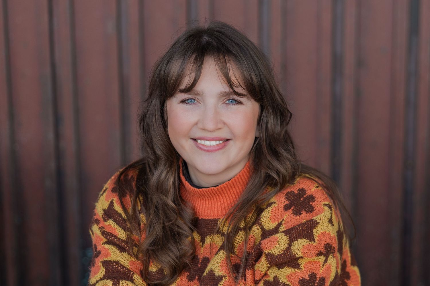 Portrait of someone wearing an autumn-themed sweater with orange and yellow leaves pattern against a dark background.