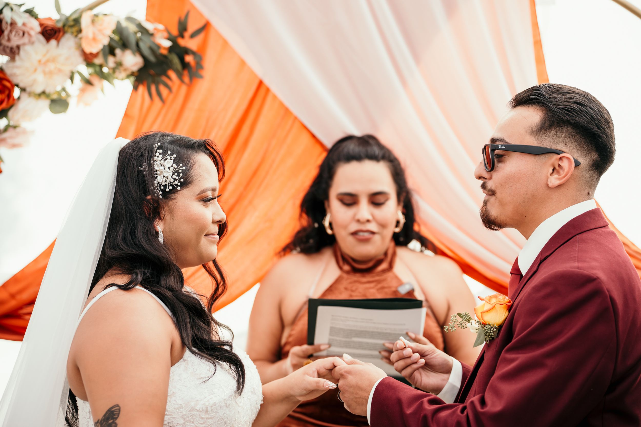 Wedding officiant with tablet guides a couple through their vows during an intimate ceremony with orange decor.