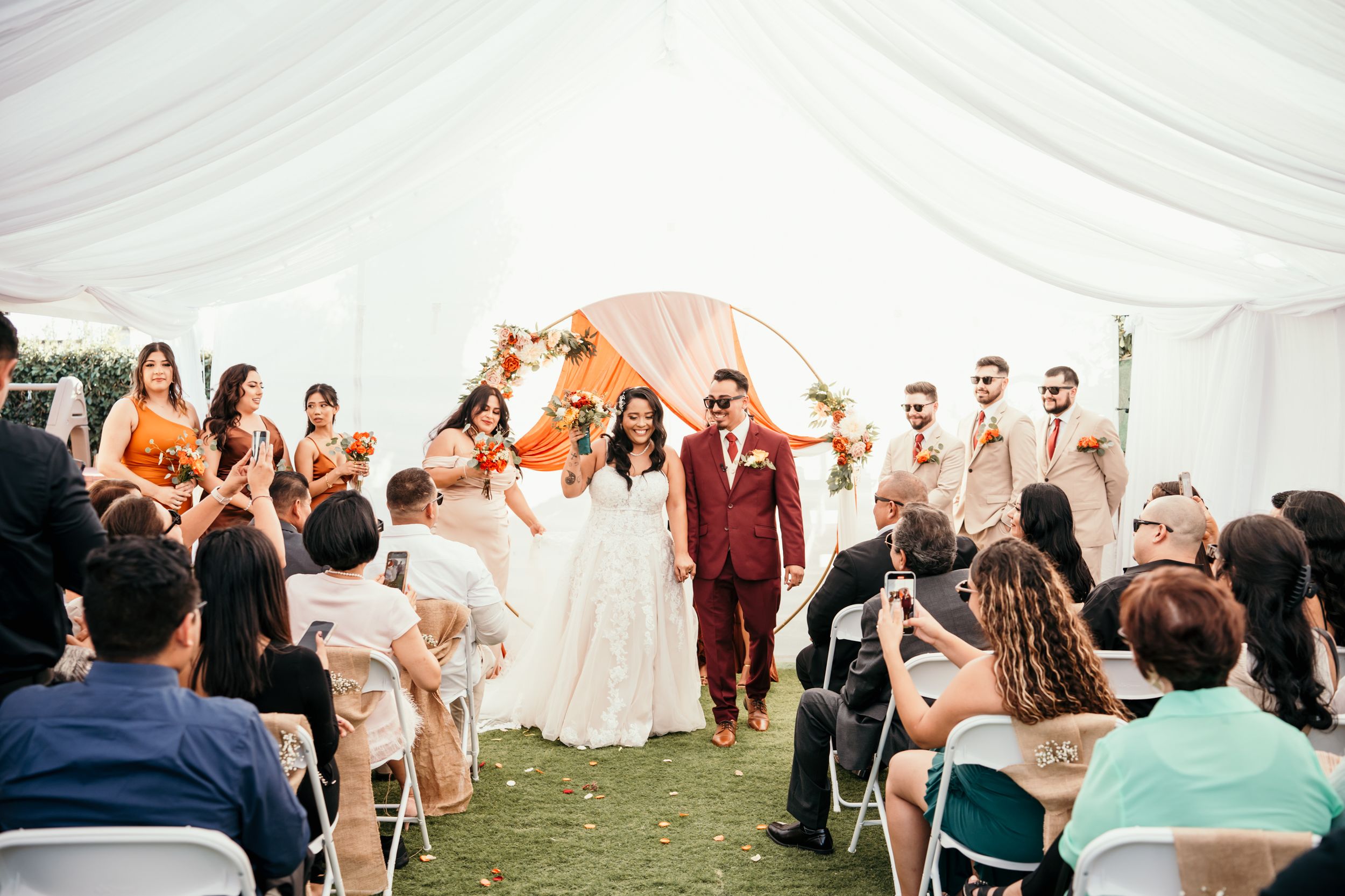 A joyous wedding ceremony under a white tent with guests seated on either side of the aisle.