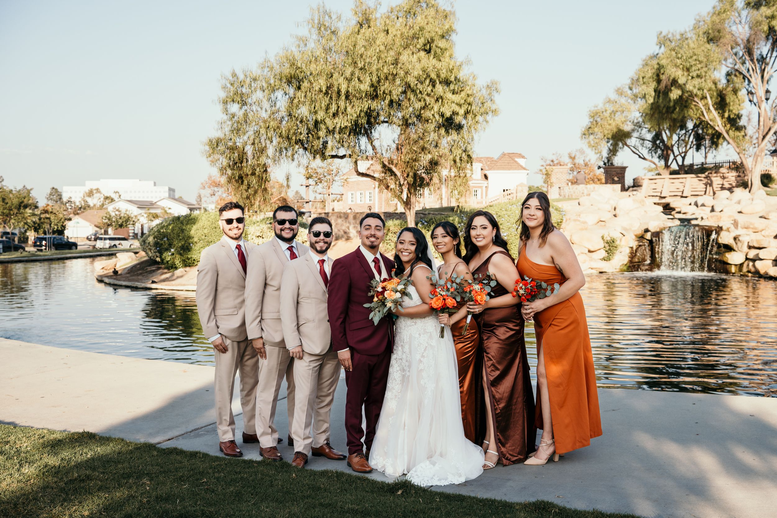 Wedding party poses together by a waterfront with bridesmaids wearing earth-toned dresses.