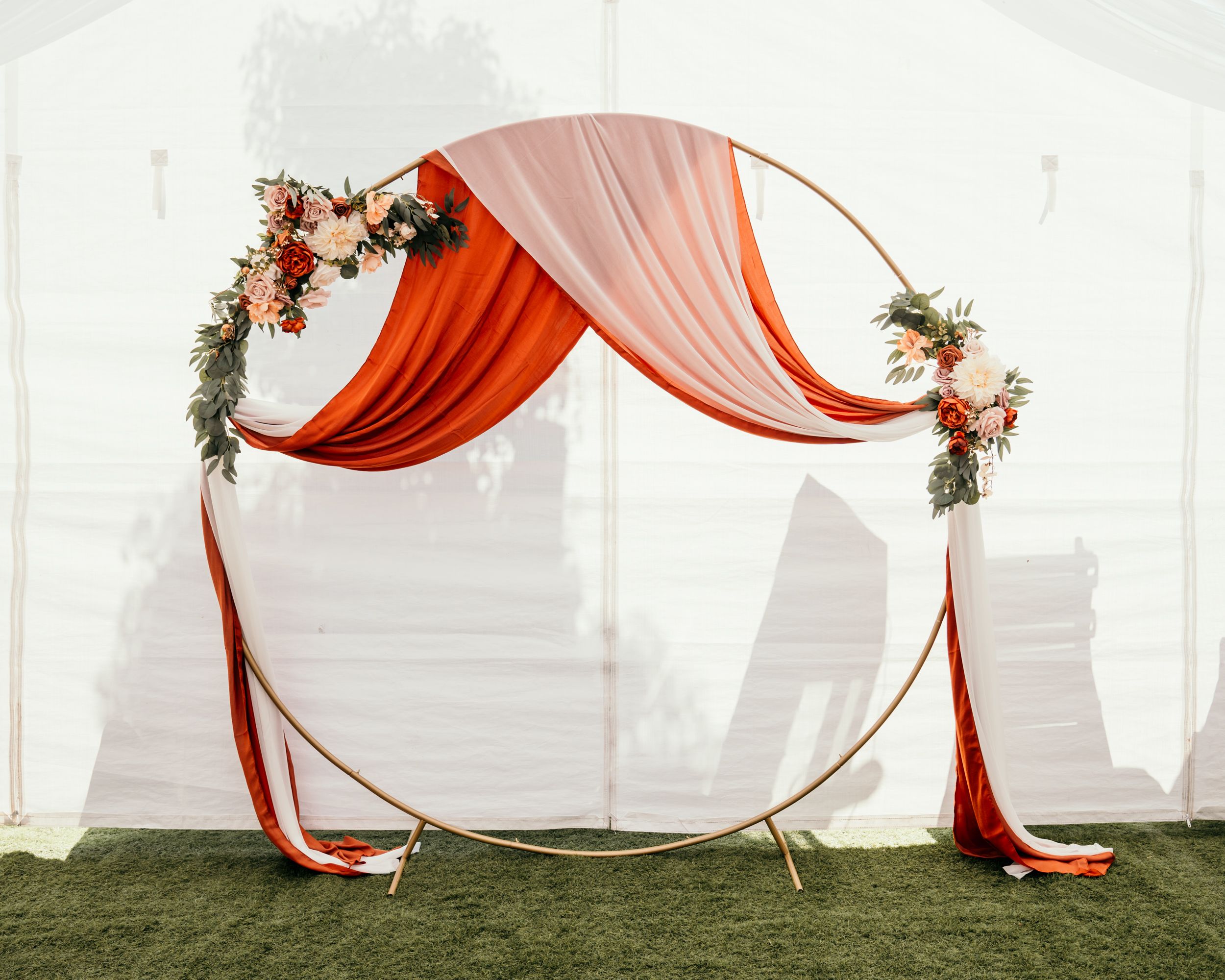 A circular wedding arch decorated with terracotta and blush pink draping fabric and floral arrangements against a city skyline.