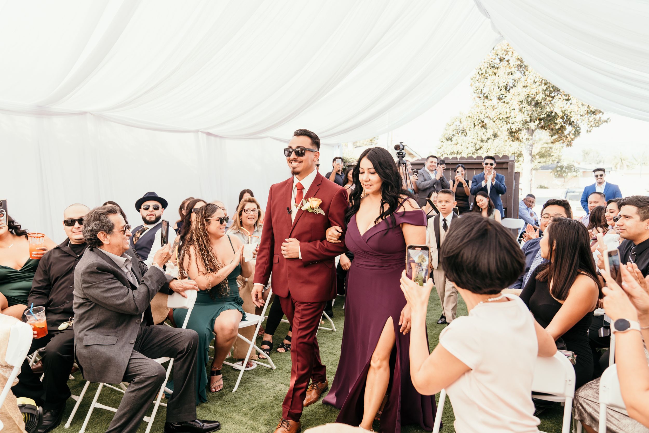 Wedding guests celebrating in a tent venue with elegant burgundy and plum attire at an outdoor reception.