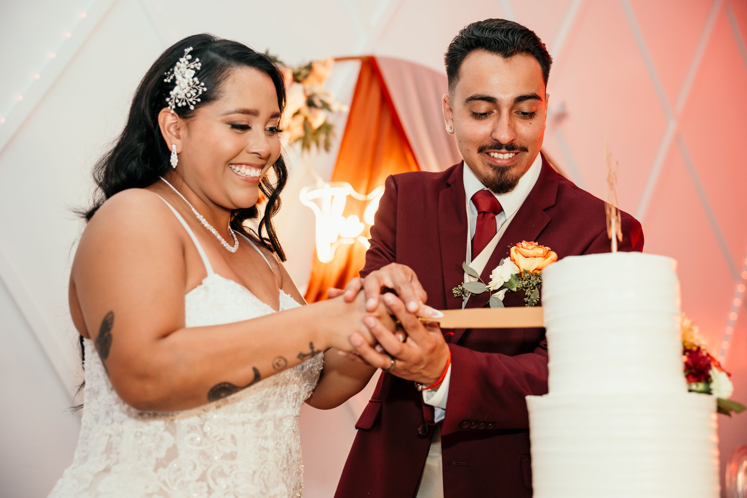 A couple cuts into their elegant white wedding cake together during their reception.