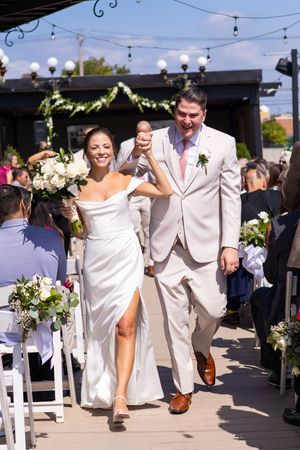 Joyful newlywed couple walks down the aisle holding hands after their outdoor wedding ceremony.