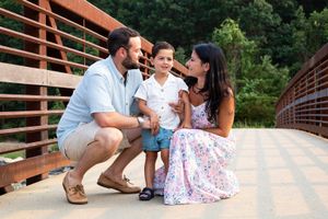 Family of three with parents and young son posing together on a wooden bridge outdoors.