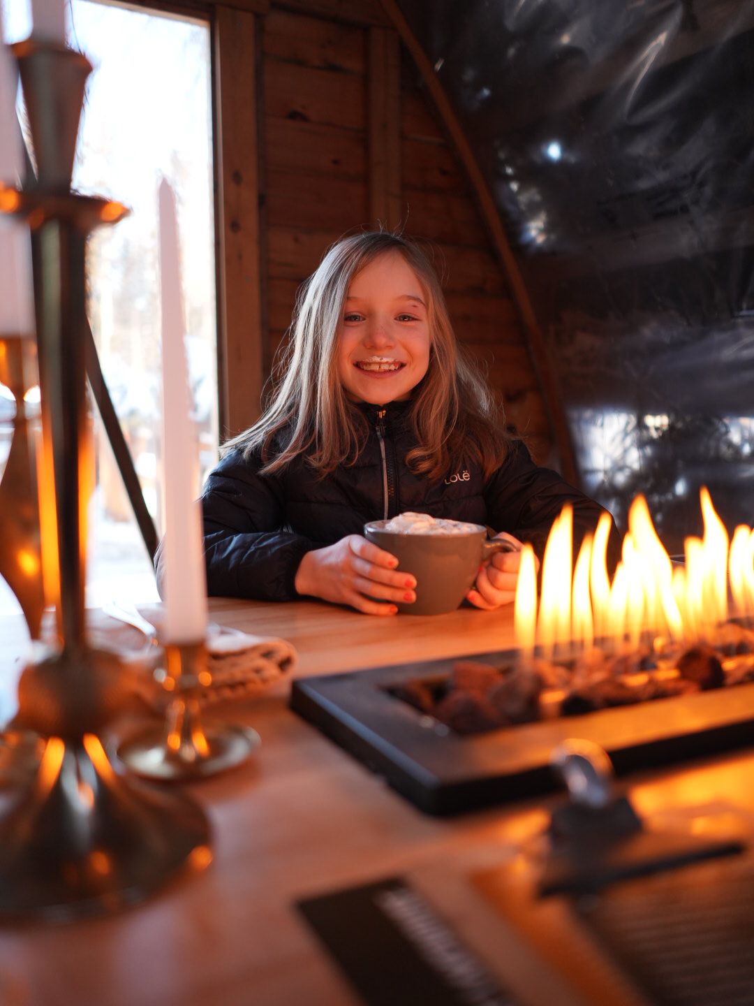 Candlelit table setting creates warm ambiance in a rustic winter cabin.