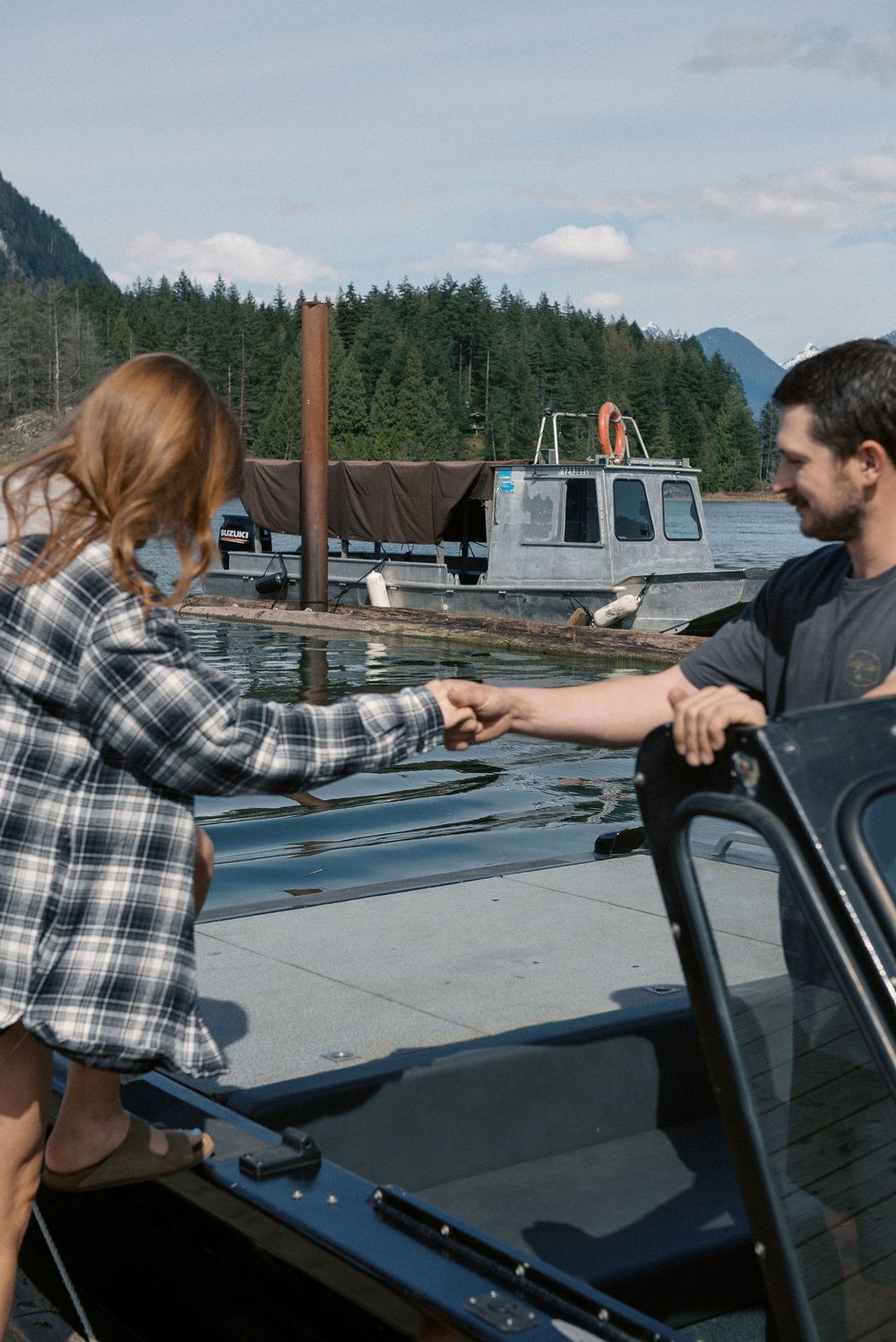 People preparing a boat at a dock with mountains and forest in the background.