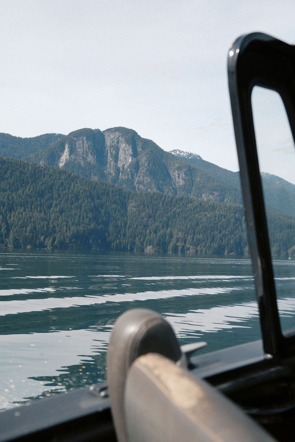 Mountain lake scenery viewed through boat windshield on calm water.