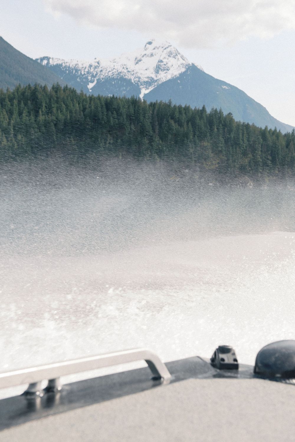 Snow-capped mountains rise above evergreen forests along a misty waterfront.