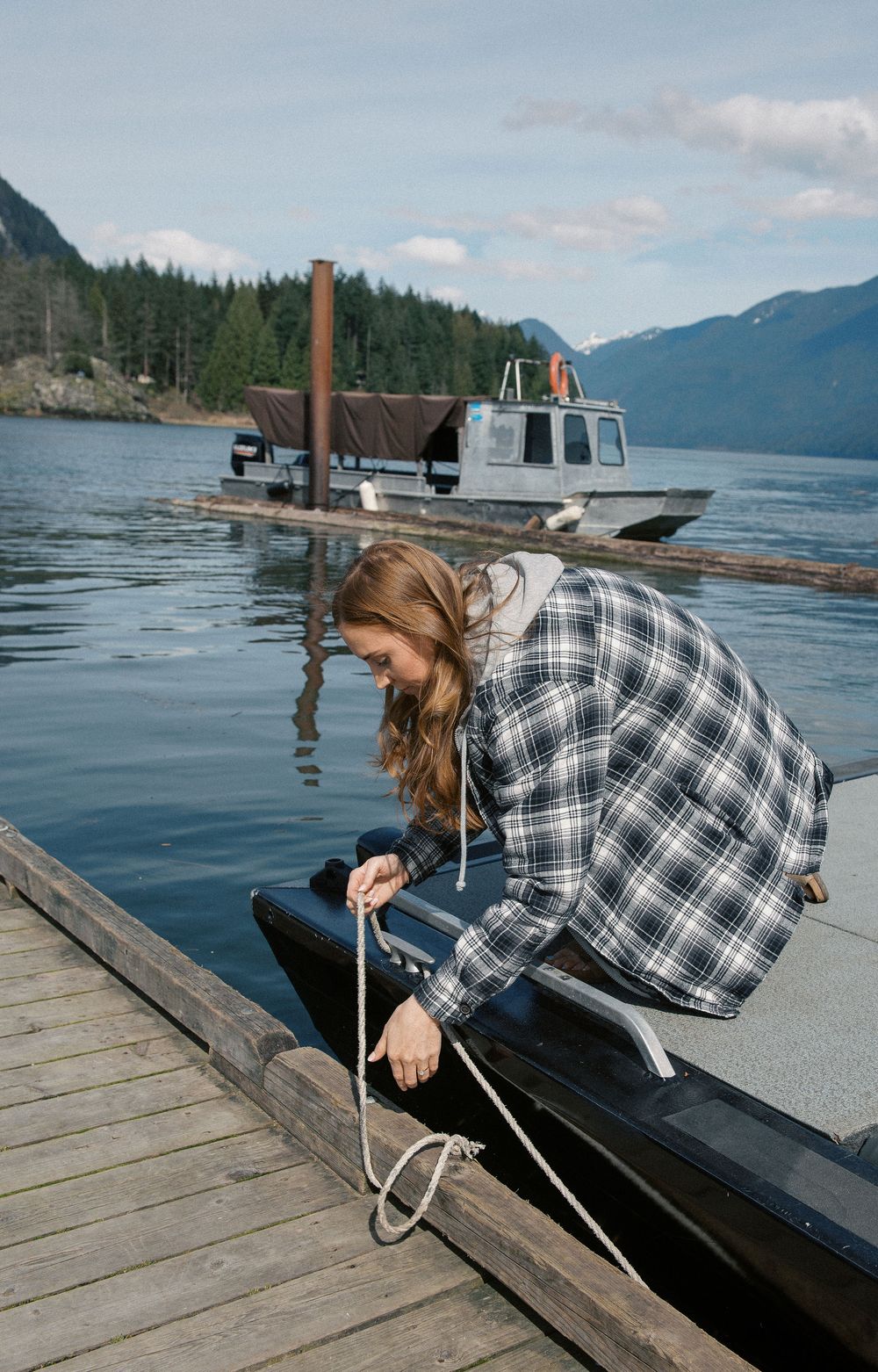 Person in plaid shirt tying rope to secure boat at mountain lake dock.