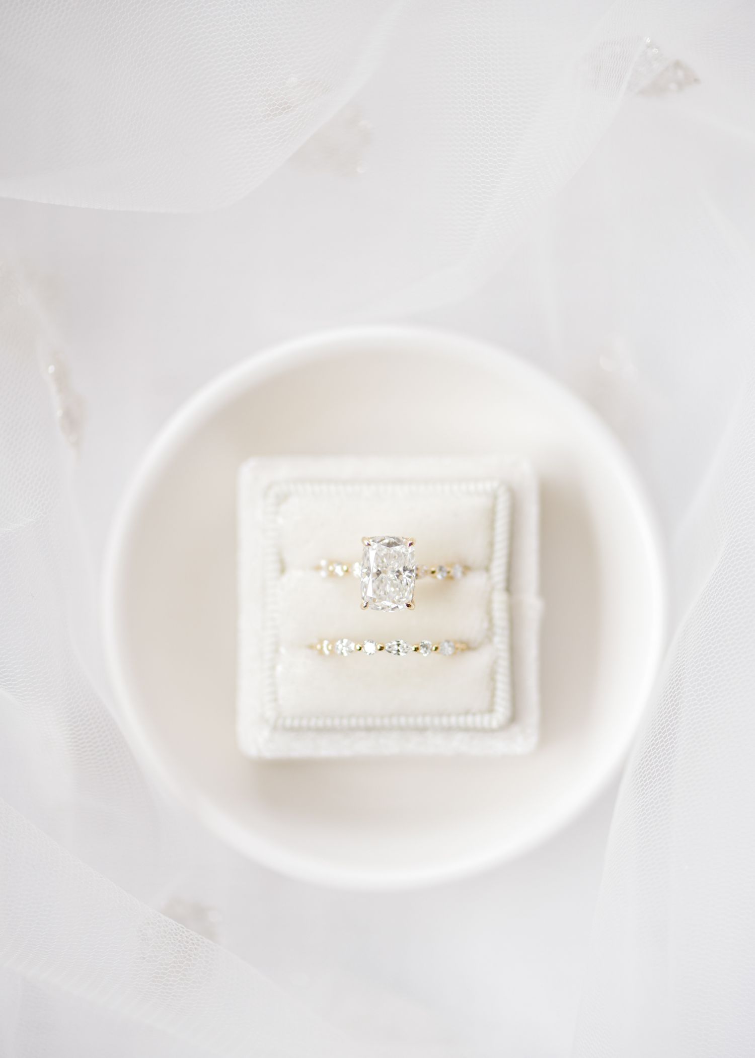 Two elegant diamond wedding rings nestled in a white velvet ring box on a ceramic plate.