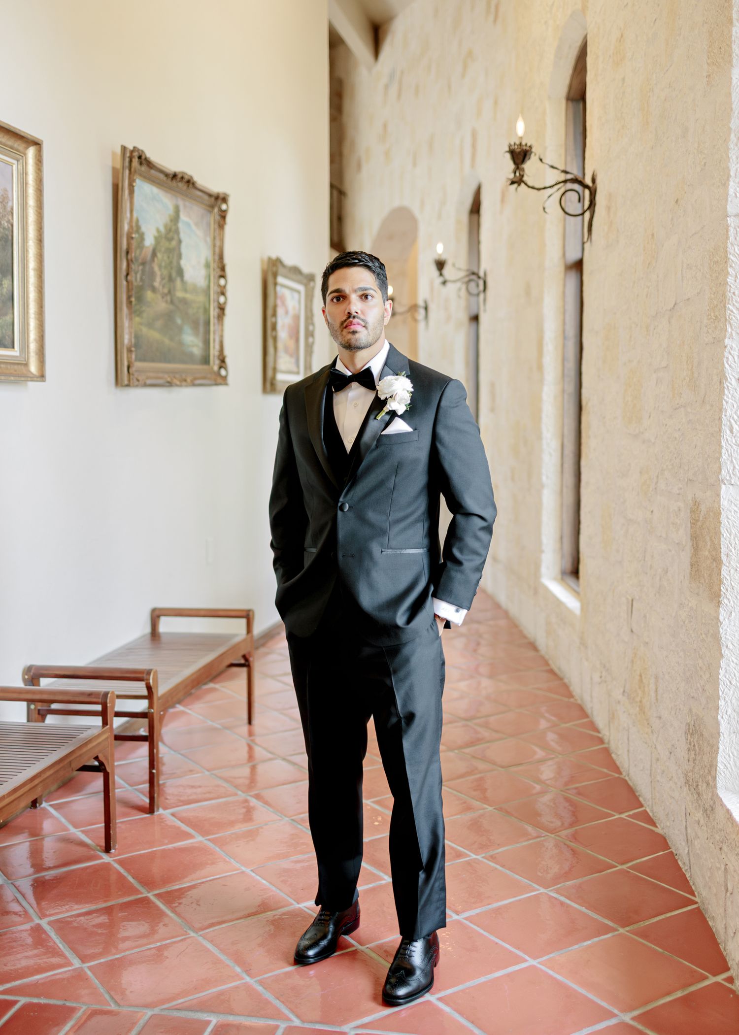 Elegant black tuxedo with boutonniere photographed in Spanish-style corridor with terracotta floors and arched walls.