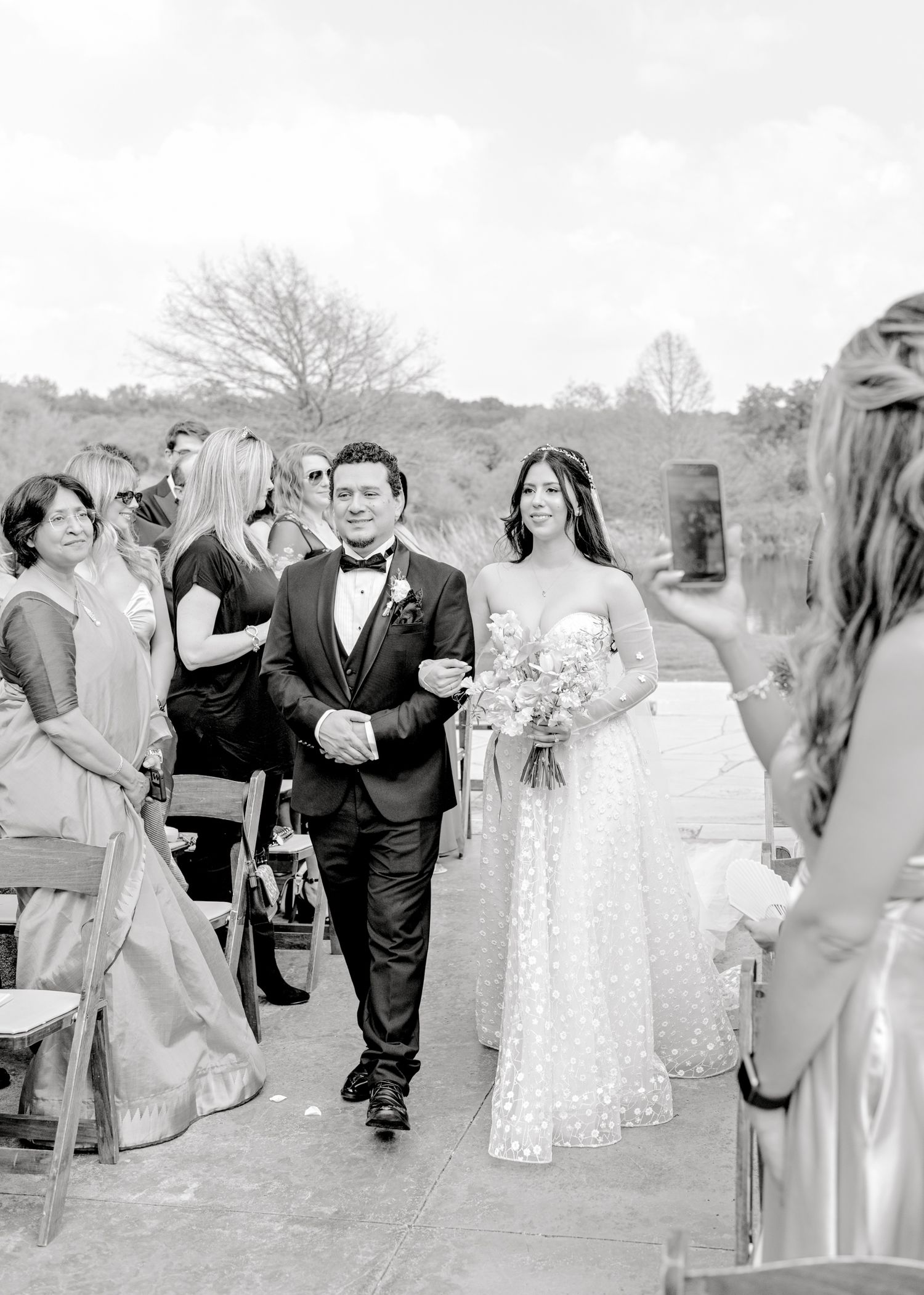 Black and white photo of an outdoor wedding ceremony walking down aisle at a garden venue.