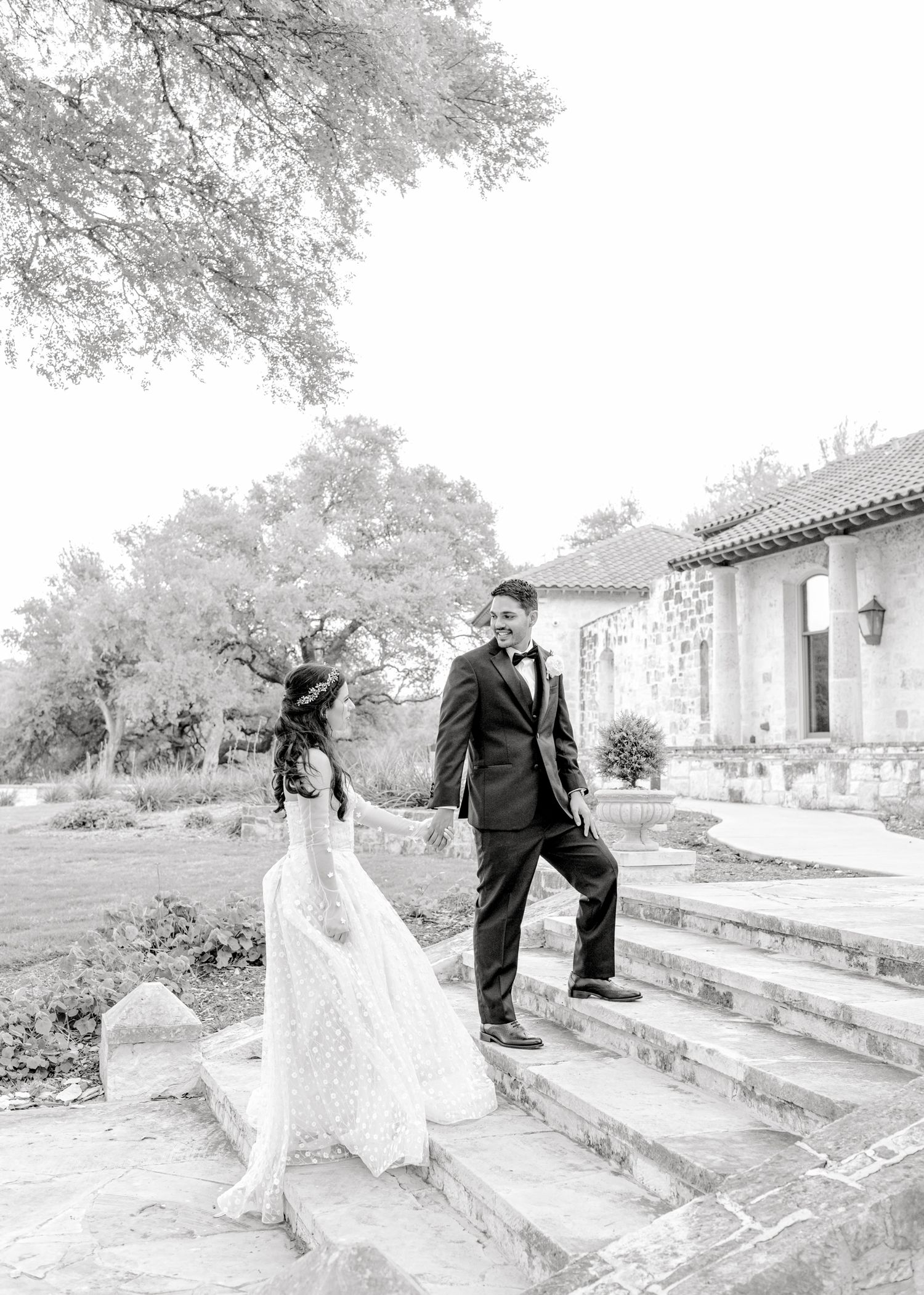 Black and white photo of couple celebrating on stone steps near Mediterranean architecture.