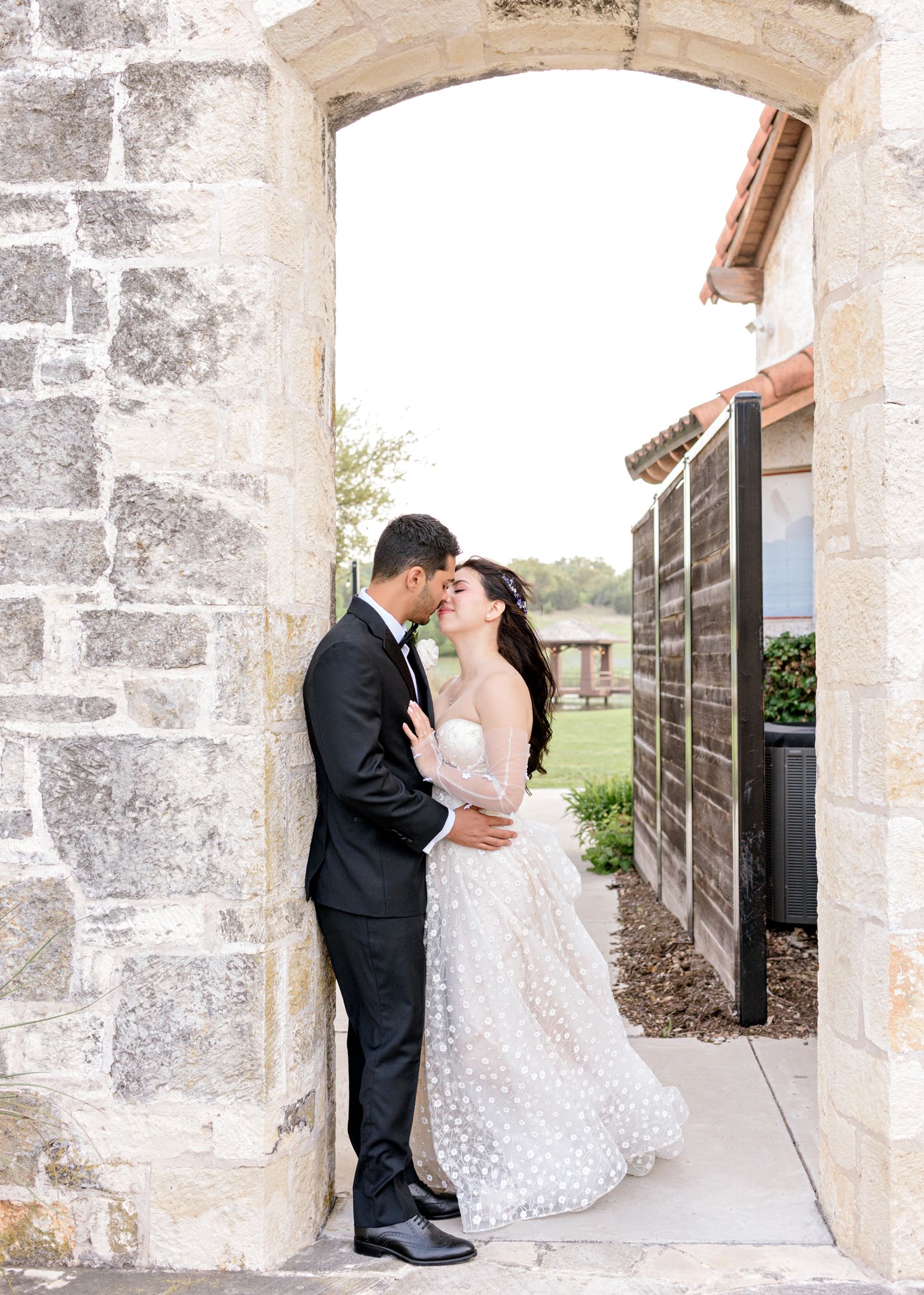 Couple shares intimate moment in stone archway of Spanish-style building.