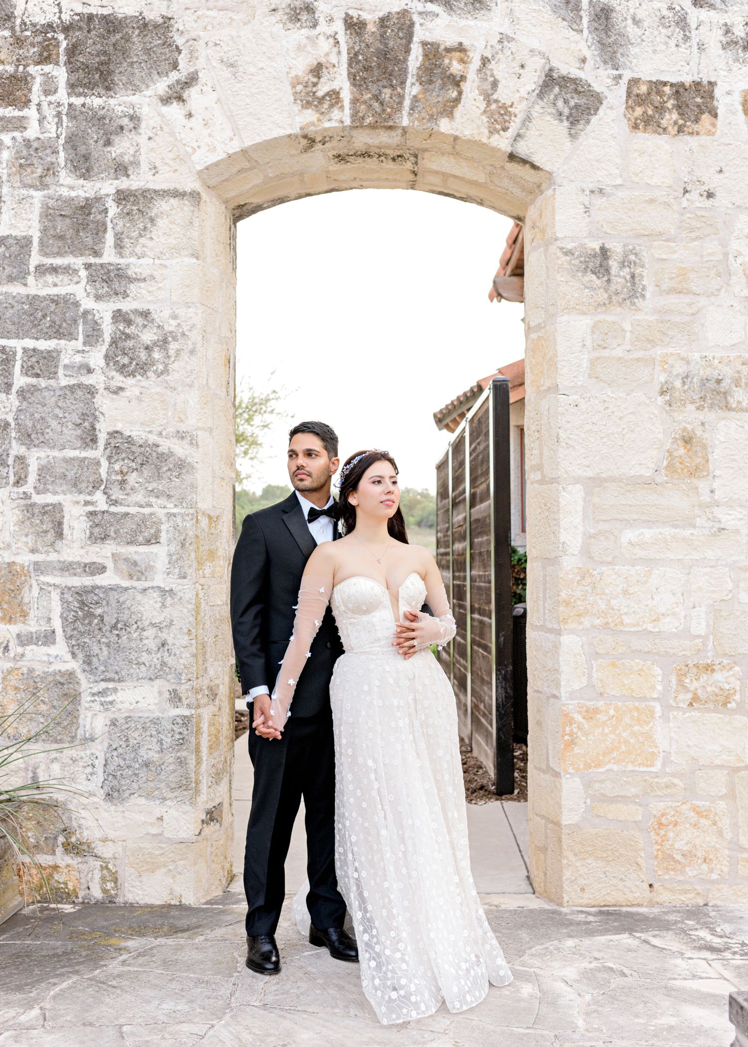 A couple stands in an elegant stone archway while wearing formal attire.