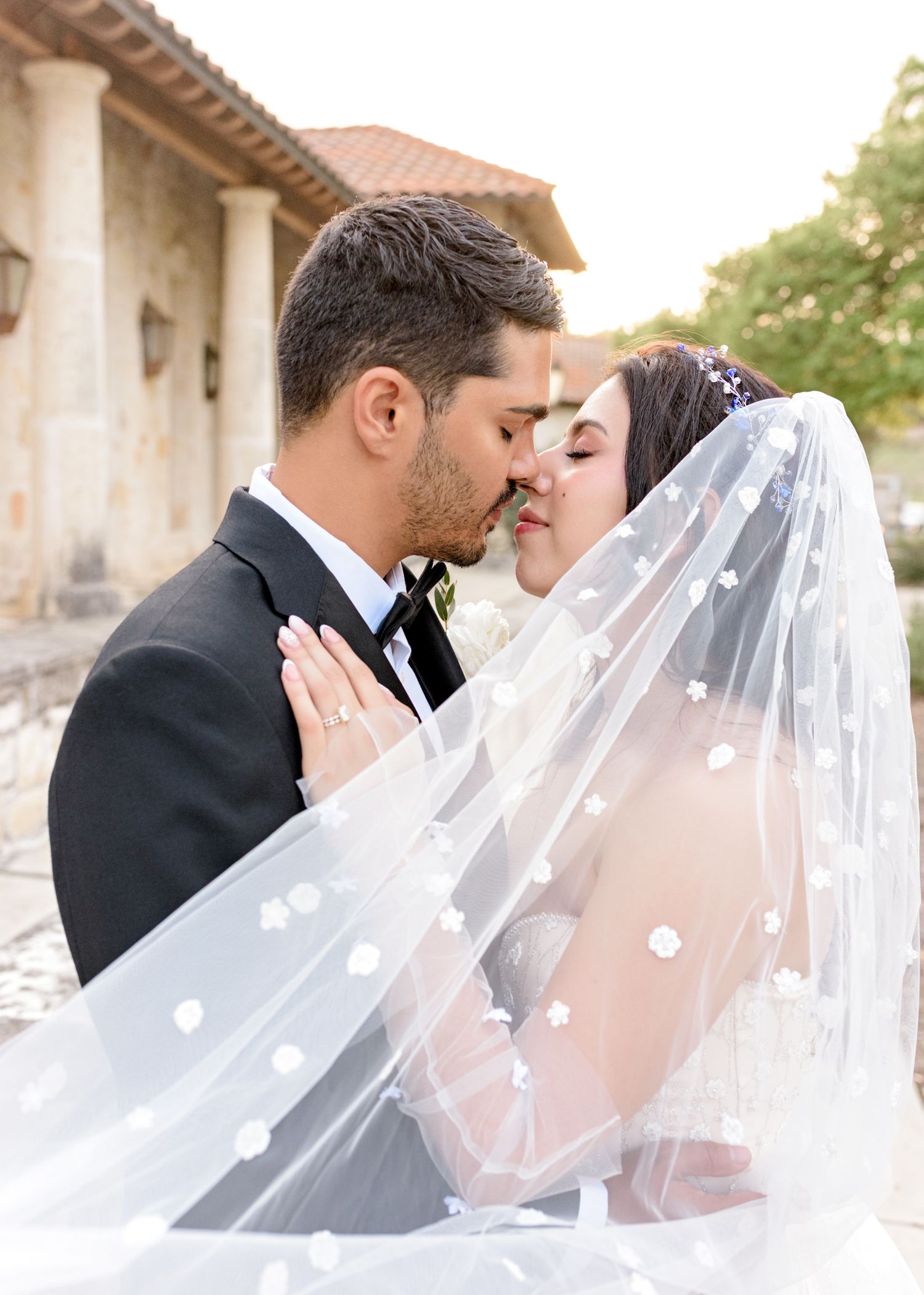 A romantic wedding couple shares an intimate moment as the bride's delicate dotted veil flows in the sunlight.