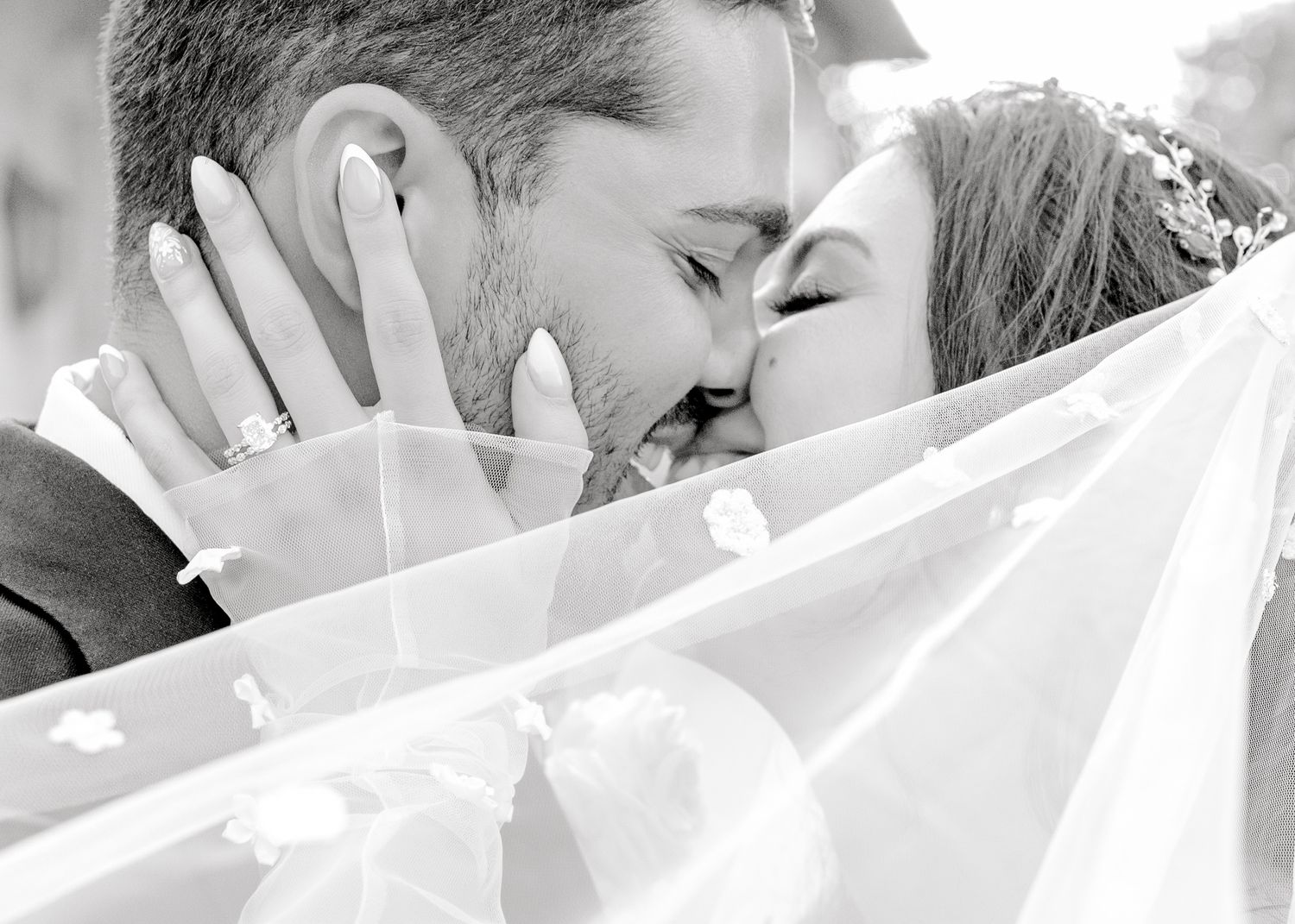 Black and white portrait of couple sharing kiss behind delicate wedding veil.