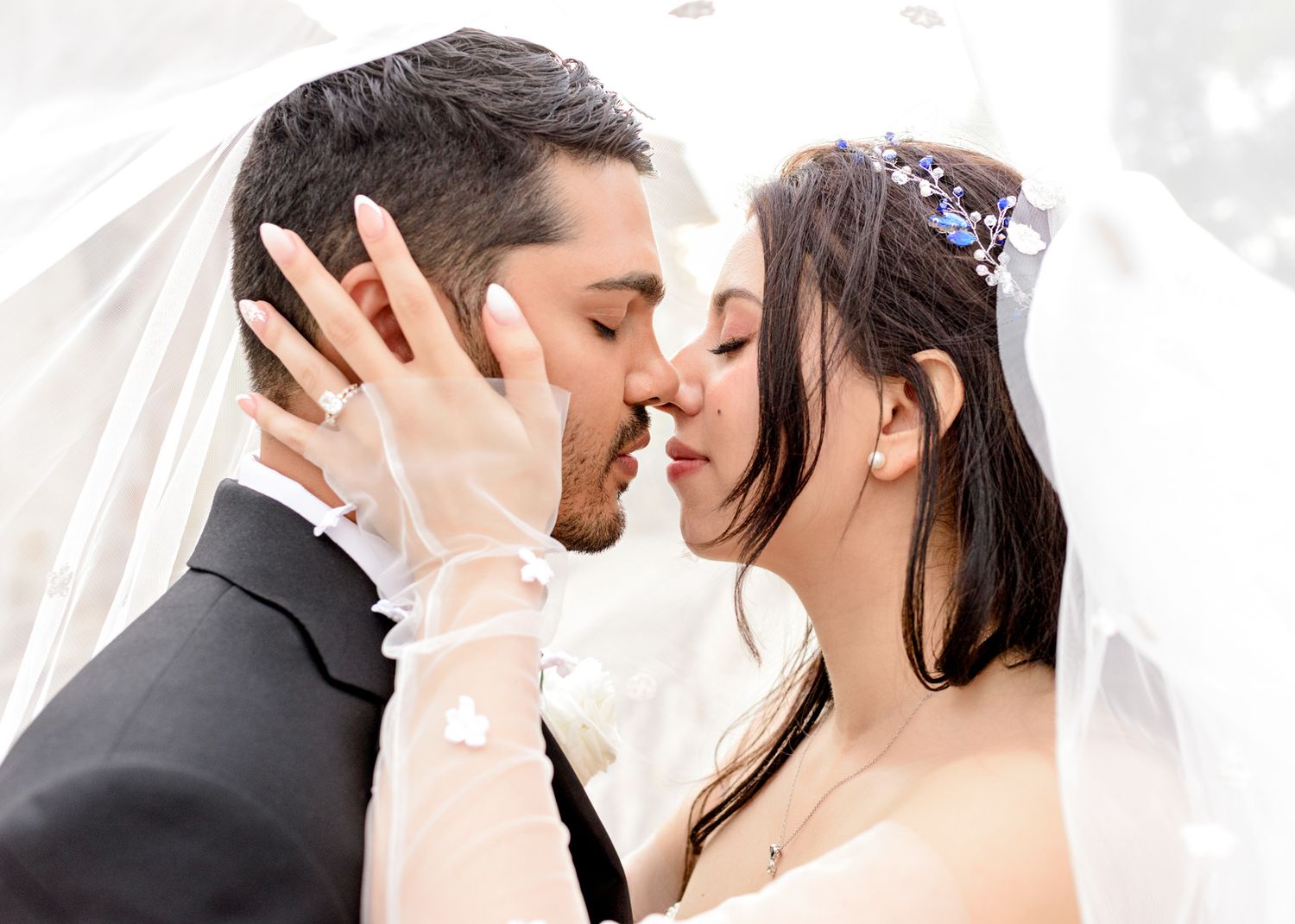 A romantic couple share a tender kiss at their wedding ceremony under a flowing white veil.