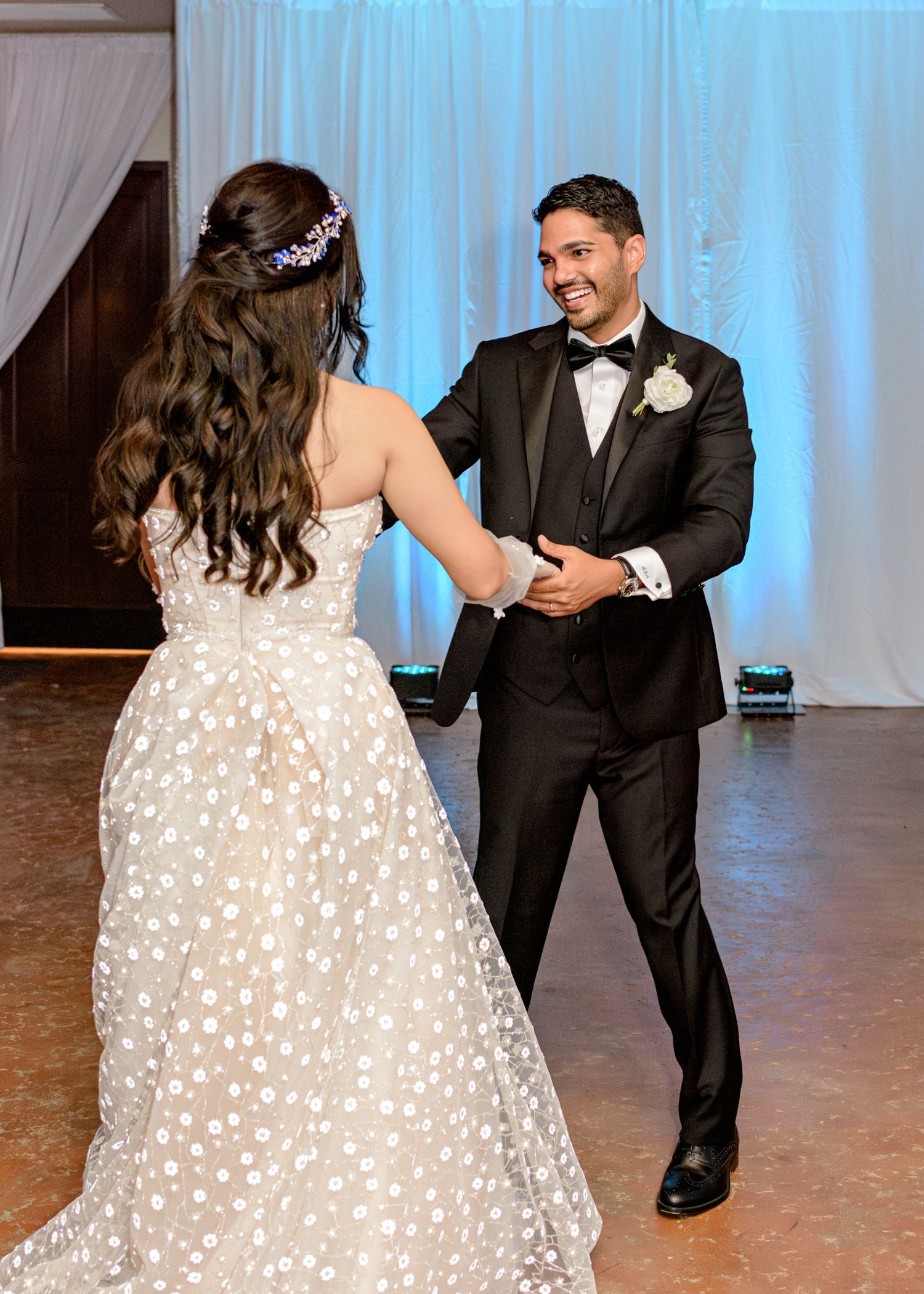 A bride in a sparkling polka dot gown shares a dance with her partner in a black tuxedo at their wedding reception.