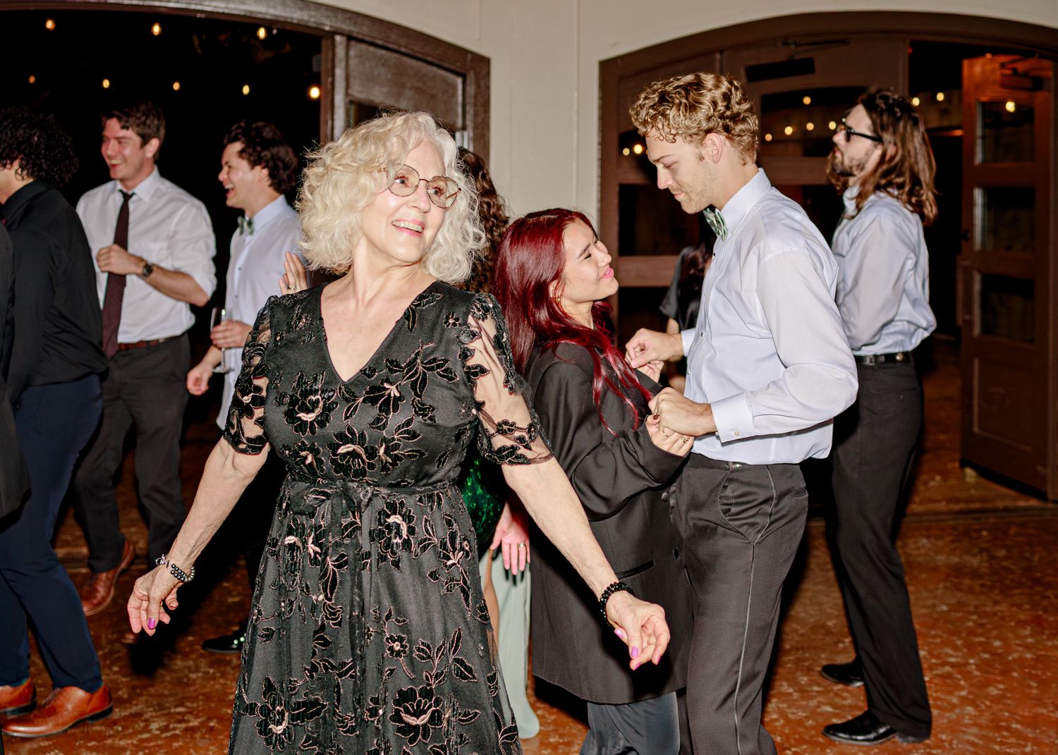 People dancing together in formal attire at an evening party with dimly lit ambiance and sparkly decorations.