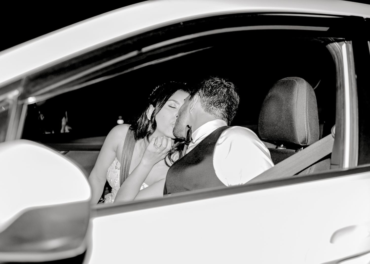 Black and white photograph showing a tender kiss between a couple inside a car.