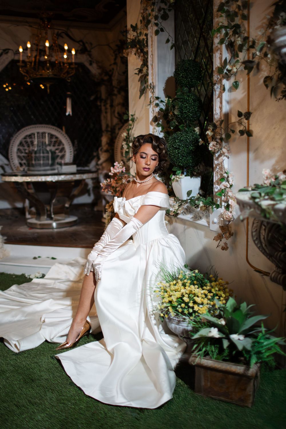 Elegant wedding dress displayed in a romantic venue with chandelier, greenery and potted plants creating an intimate atmosphere.