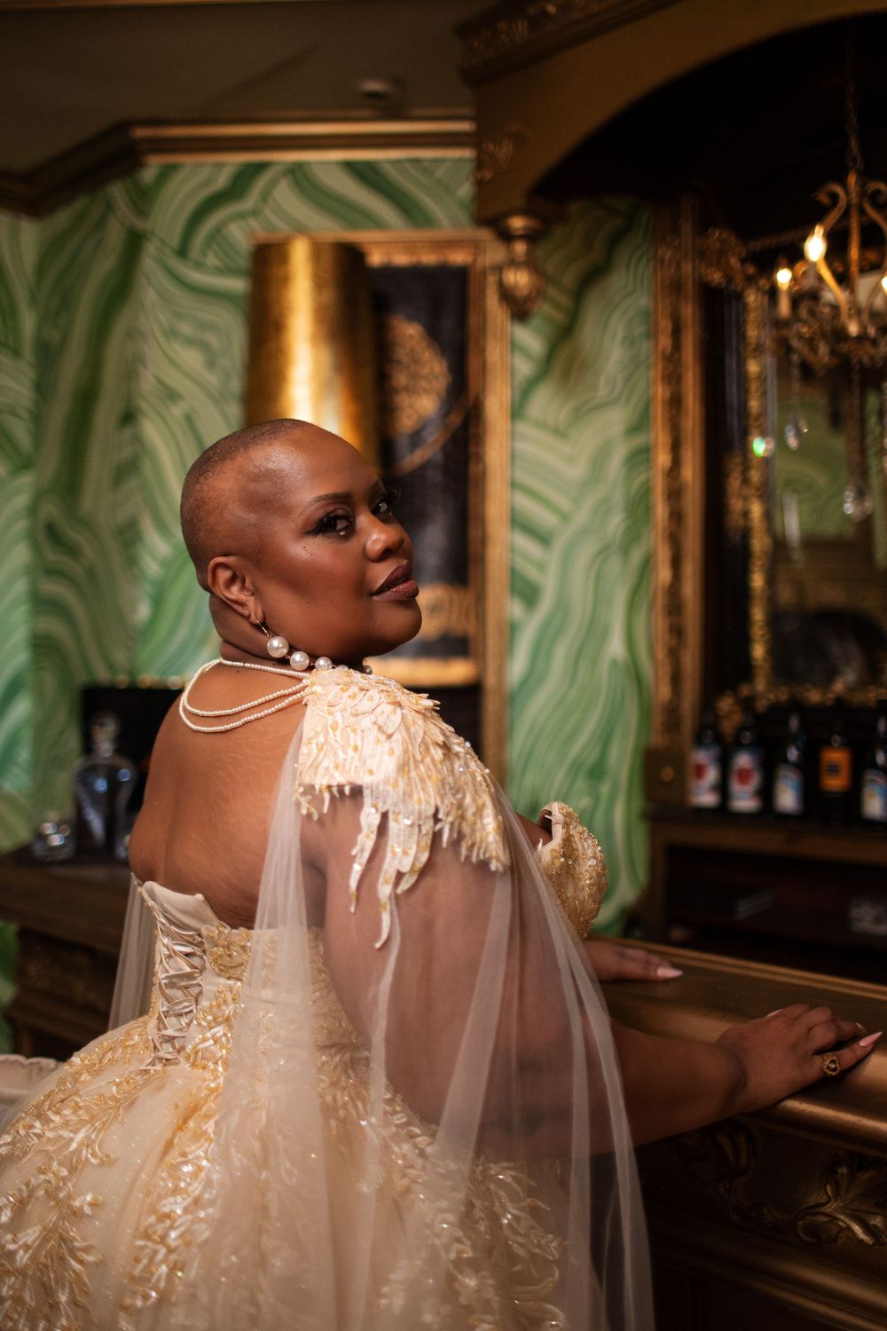 An elegant wedding dress with sheer sleeves and delicate lace detailing is showcased in a glamorous bar setting.