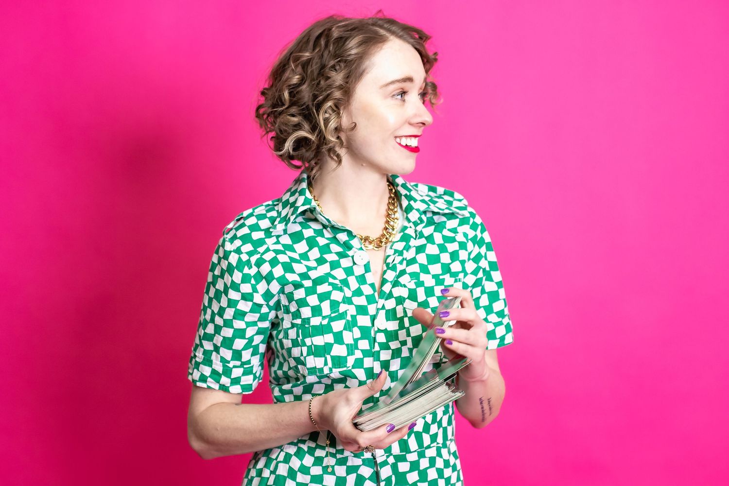 Retro-styled person in green polka dot dress stands against bright pink background looking sideways with playful expression.