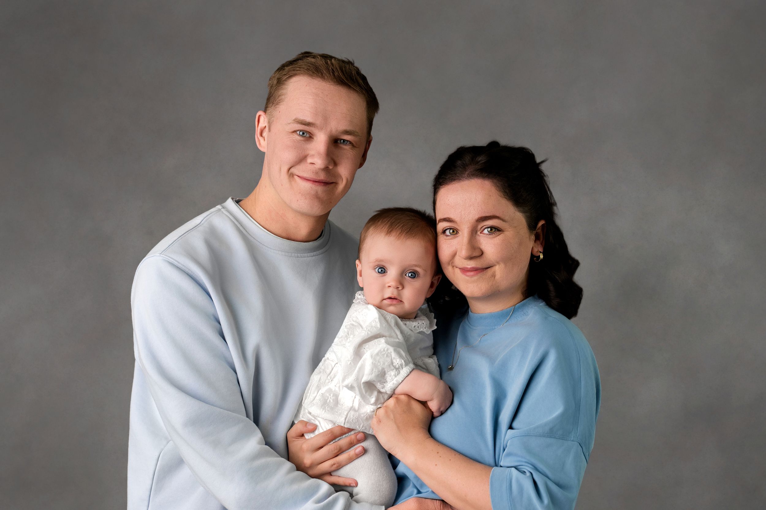 Multi-generational family wearing white clothing poses together for a formal portrait against beige background.