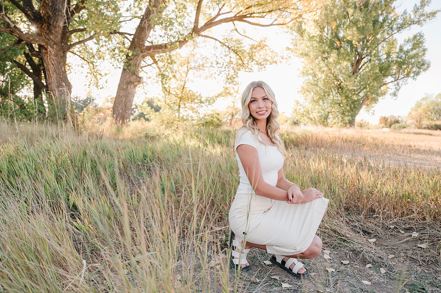 Ethereal outdoor portrait among tall grass and trees with golden sunlight filtering through the branches.